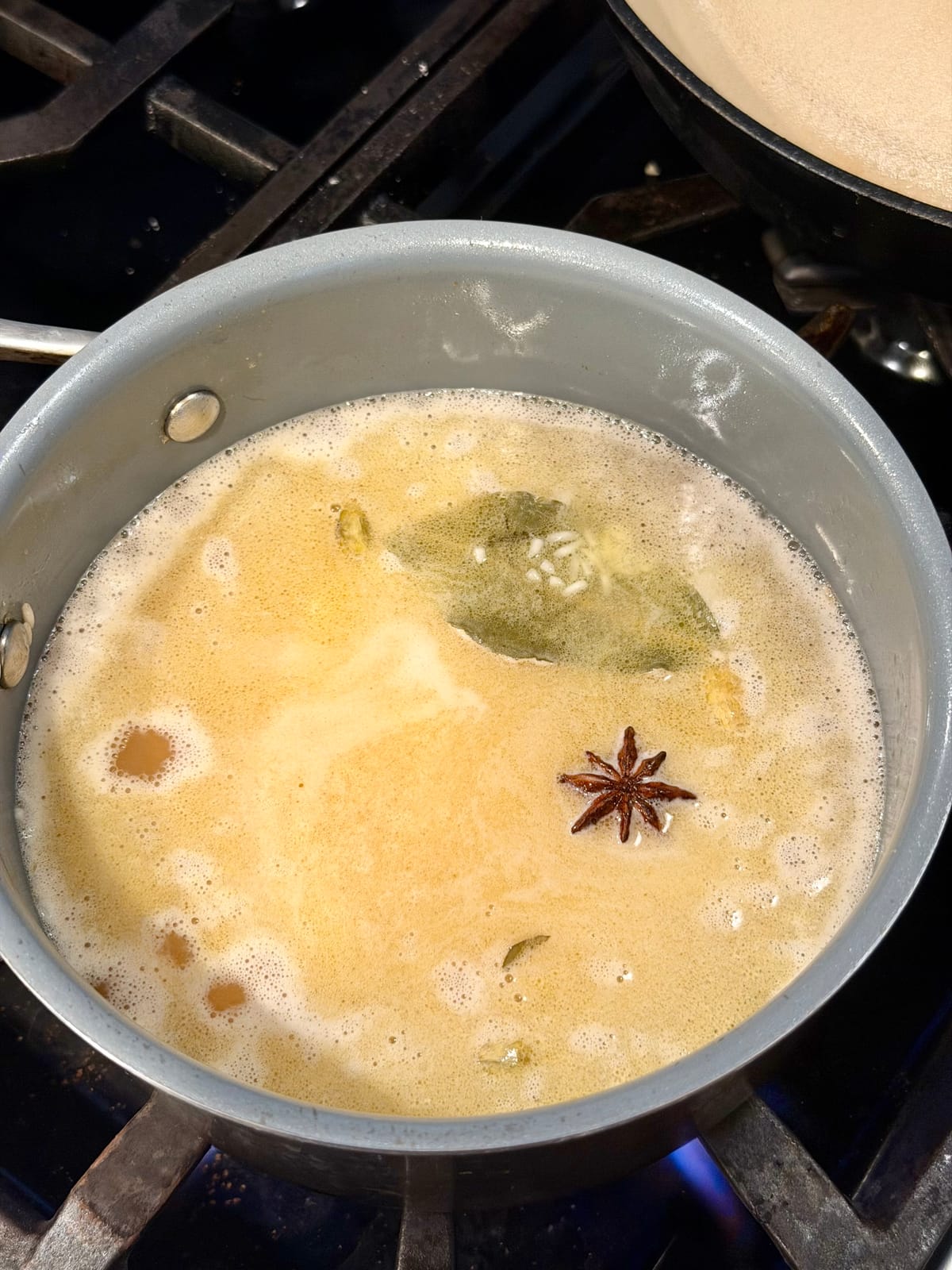Basmati rice cooking — water simmering with bloomed star anise, cardamom, and bay leaf